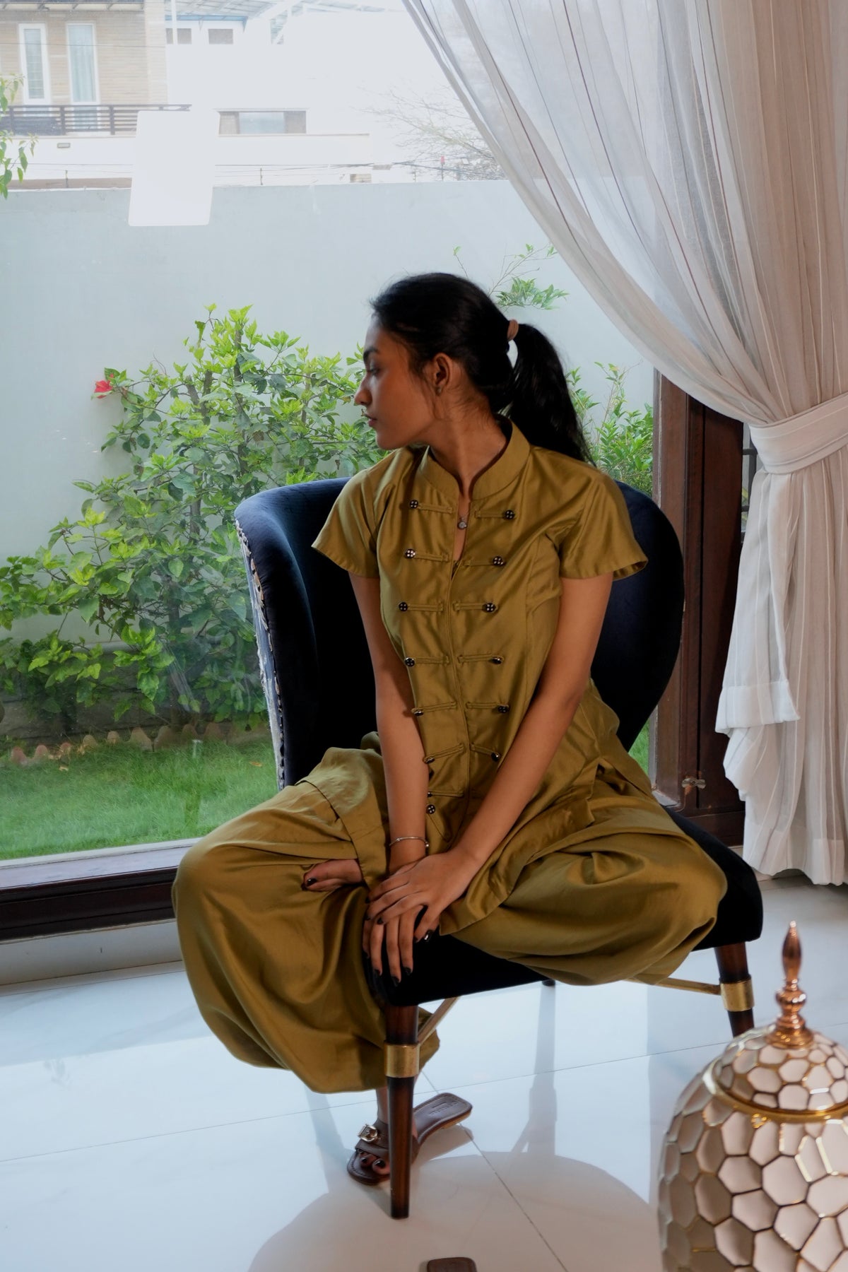 Alisho After Glow mustard Mandarin collar top and balloon pants worn by a model seated next to window